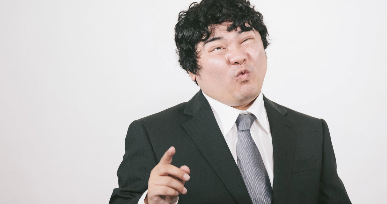 黒いスーツを着た男性が右手を前に出して大声で怒鳴っている