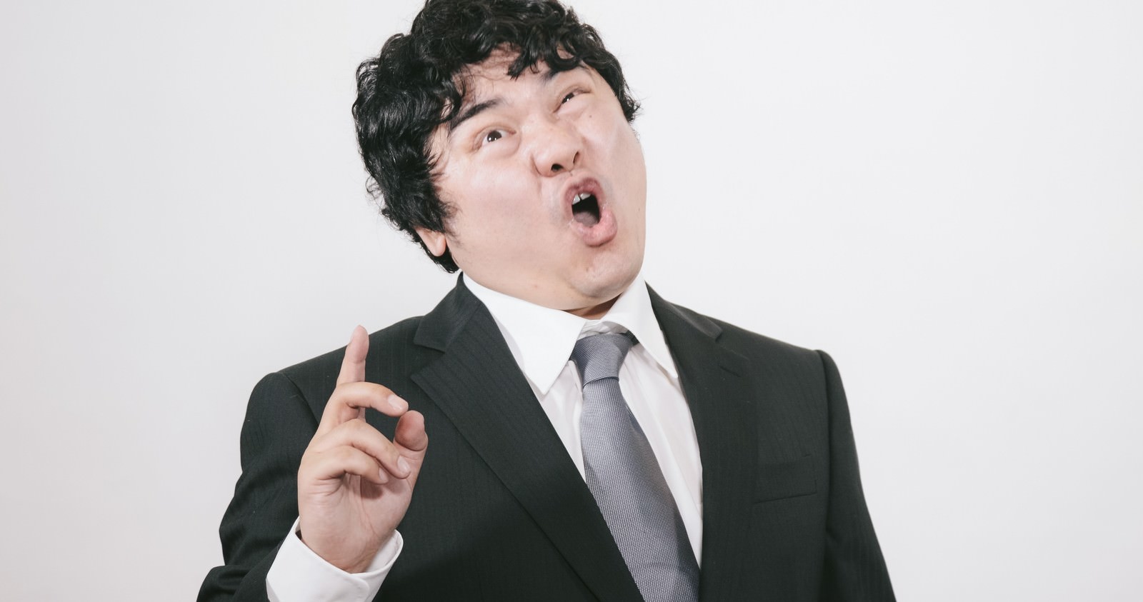 スーツを着た男性が口を開けて激怒し、左手を指して叫んでいる［モデル：段田隼人］
