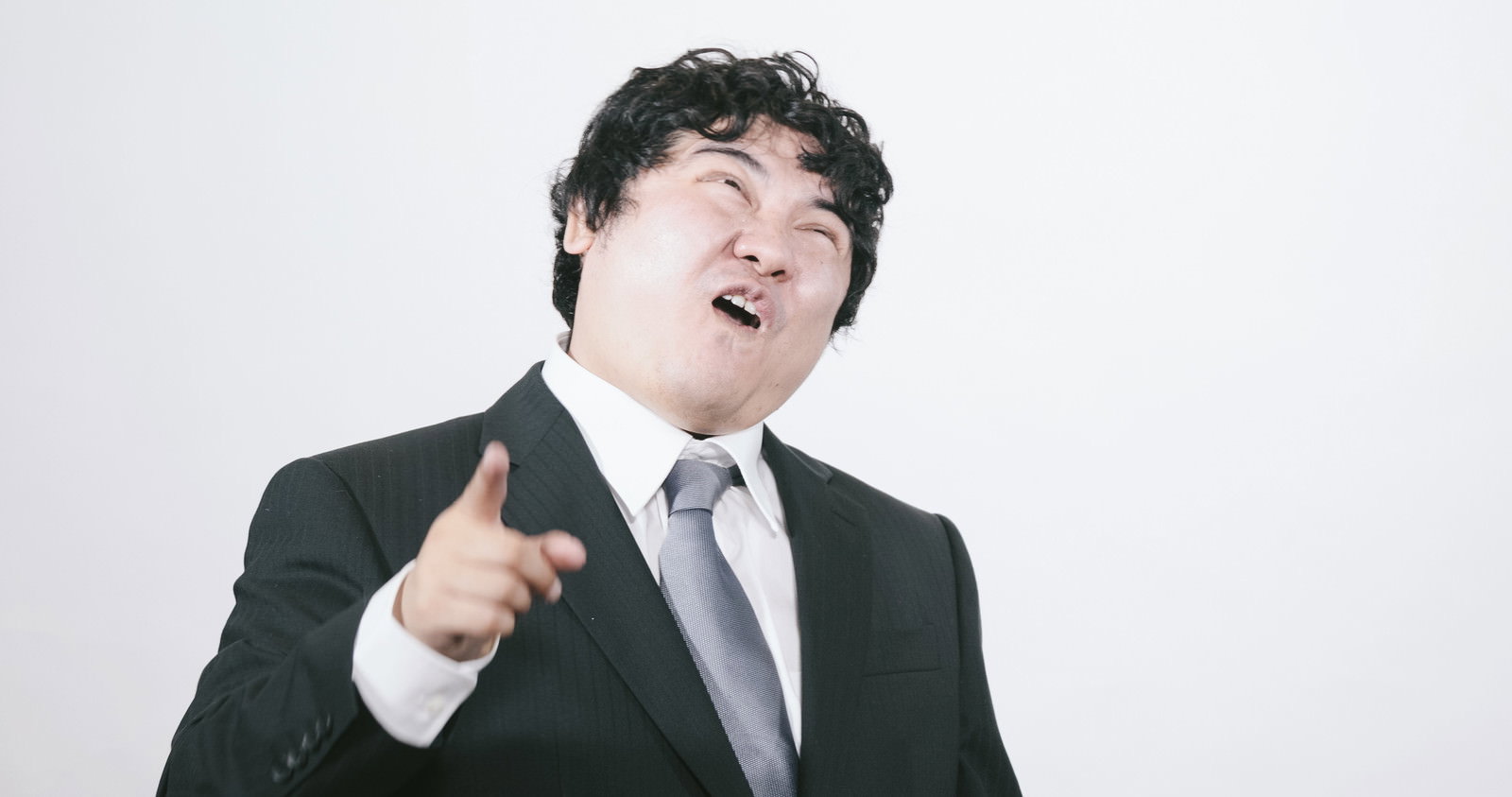 発狂して指を突きつけるスーツの男性［モデル：段田隼人］