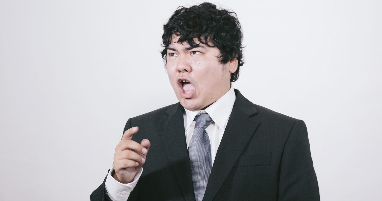 スーツを着た男性が口を大きく開けて発狂している［モデル：段田隼人］
