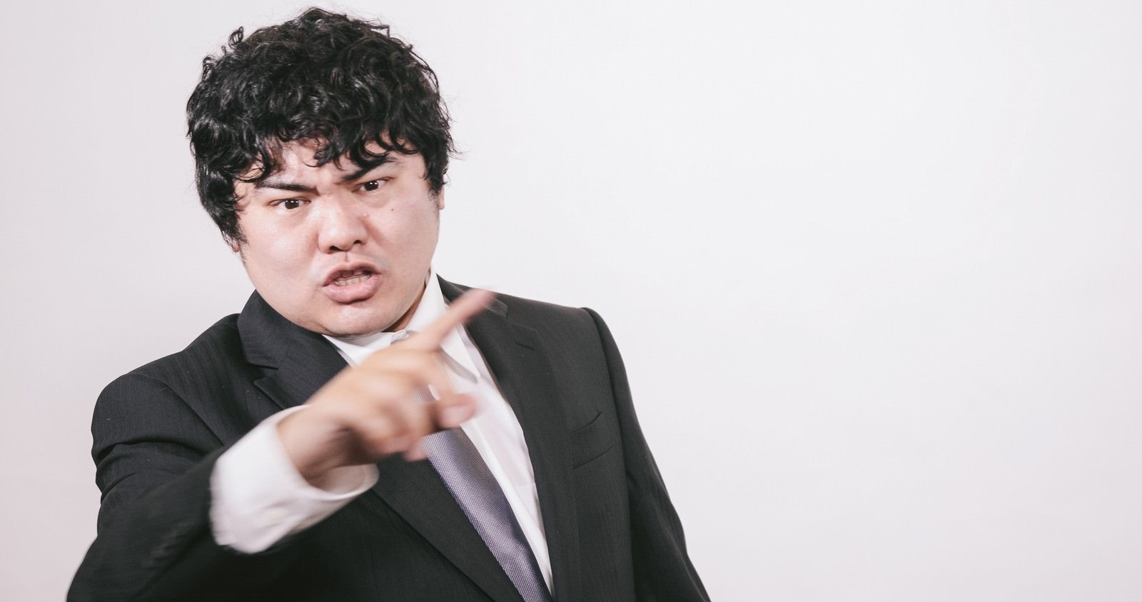 黒いスーツを着た男性が人差し指で指摘している［モデル：段田隼人］