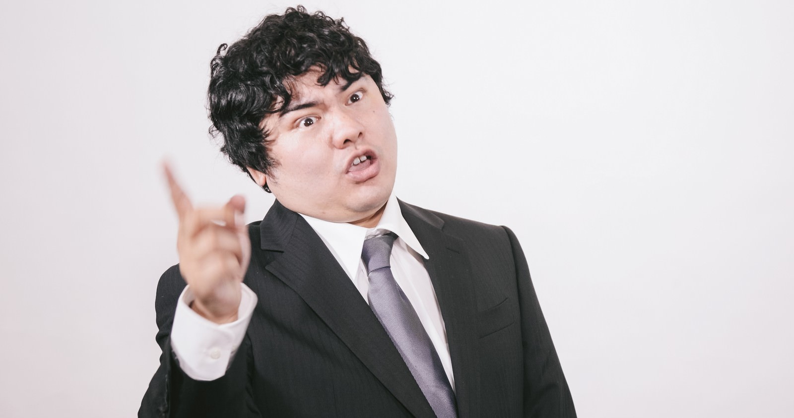 黒いスーツの男性が指を差し上げながら怒りの表情で話している［モデル：段田隼人］