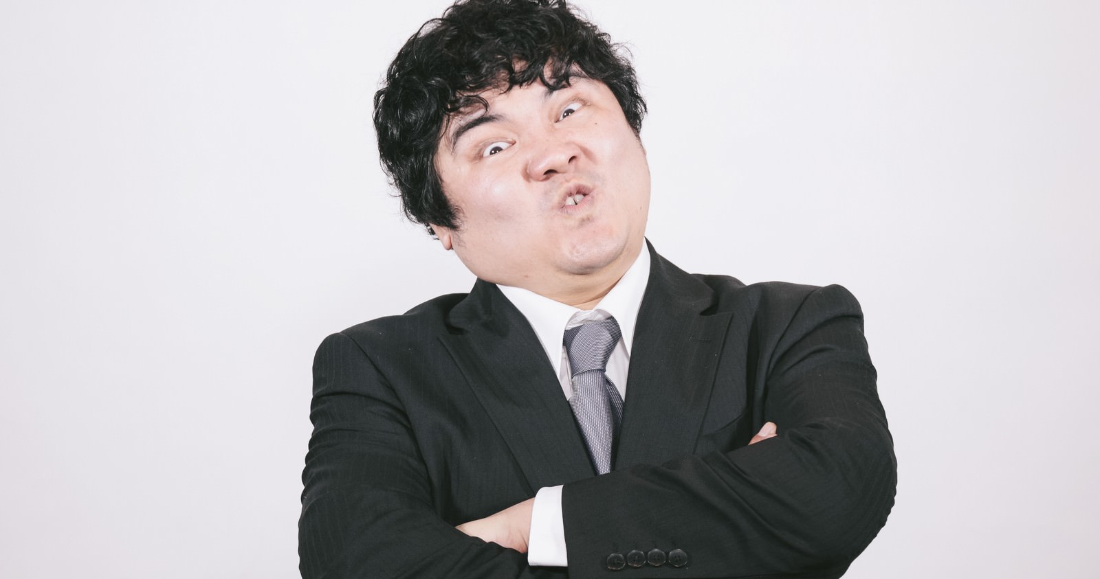 黒いスーツの男性が両腕を組み、頭髪を逆立てて上を向きながら怒りの表情を浮かべている［モデル：段田隼人］