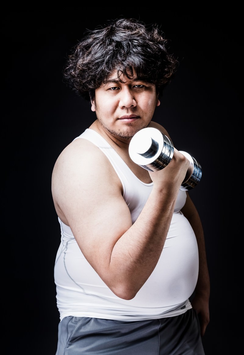 Photo of an overweight man exercising with dumbbells in a gym