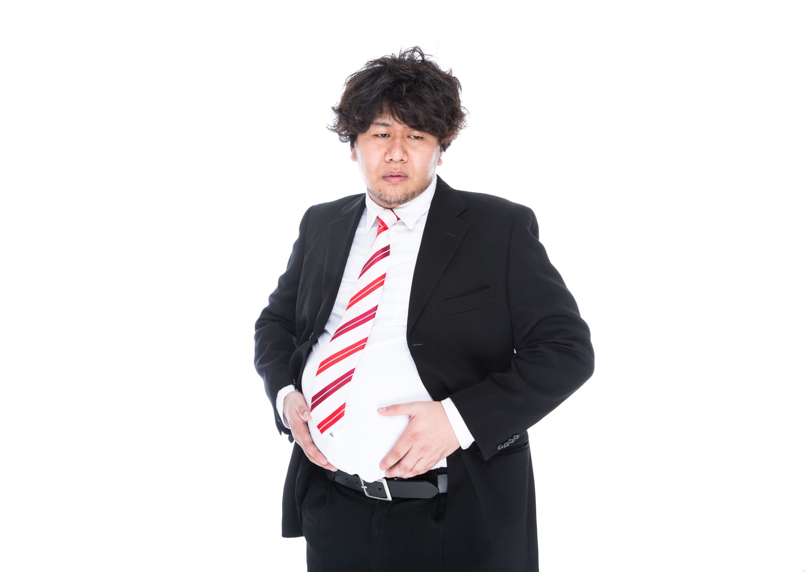 黒スーツに赤ストライプネクタイを着けた男性が、膨らんだ腹部を両手で抱えている［モデル：朽木誠一郎］
