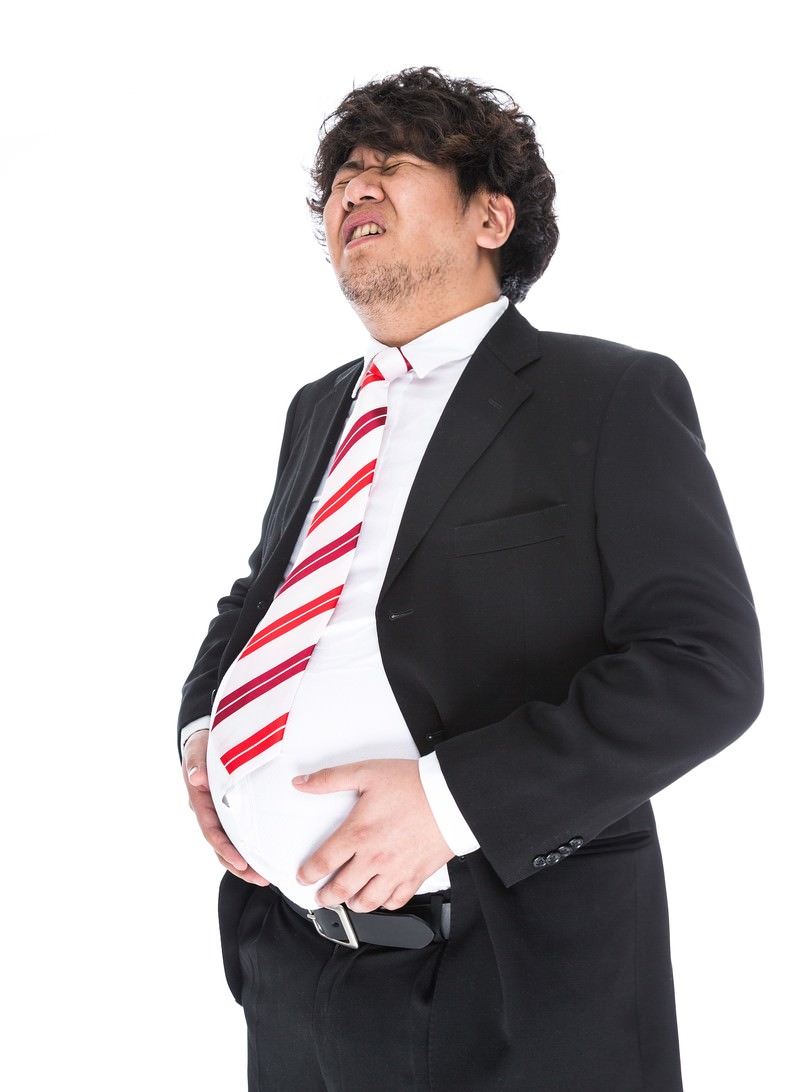 黒いスーツの男性が苦しそうな表情でお腹を抱えている［モデル：あまのじゃく］