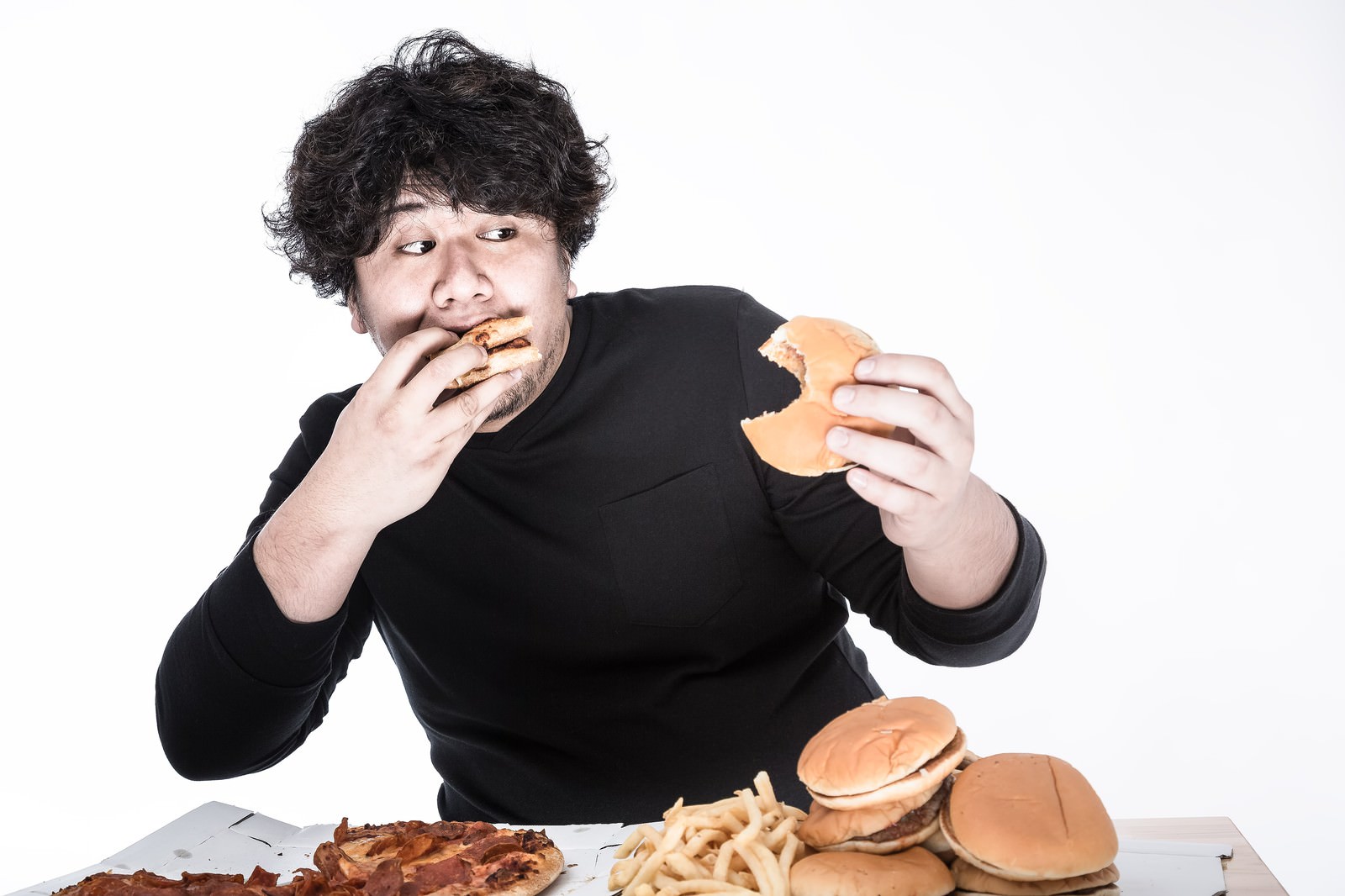 ハンバーガーとポテトフライを前にリズミカルに食べる男性［モデル：朽木誠一郎］
