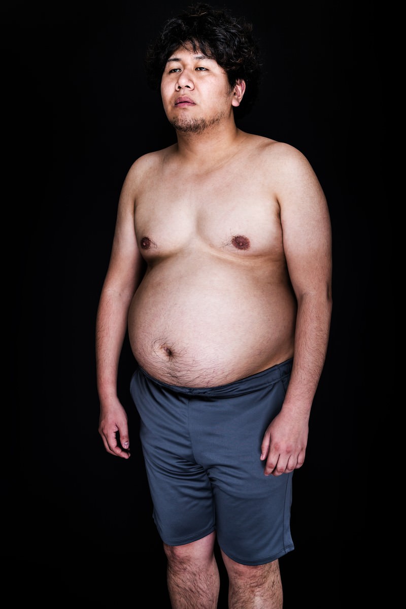 肉体改造を妄想する肥満体の男性が上を向いて立っている写真［モデル：朽木誠一郎］