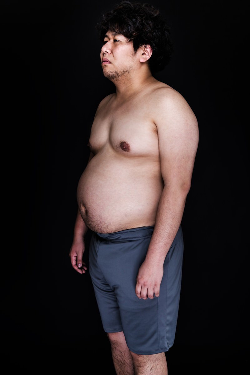 前かがみの猫背姿勢で立つぽっちゃり体型の男性［モデル：朽木誠一郎］