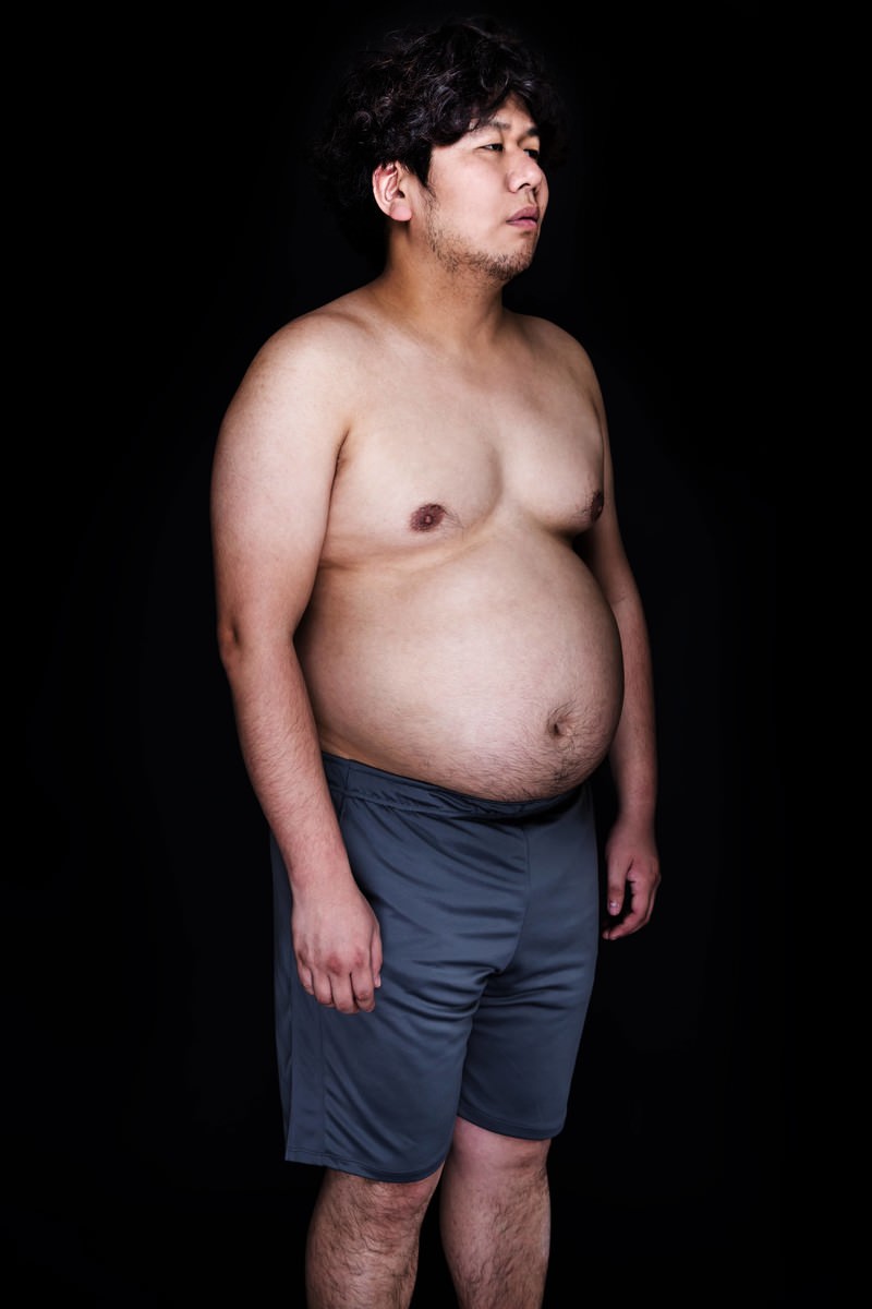 上半身を露出した男性が不安げな表情で斜め上を見つめており、腹部に皮下脂肪が付いている［モデル：朽木誠一郎］