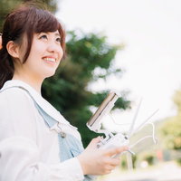 ドローンを操縦するタブレット片手の女性（ちょっとまぶしい）の写真