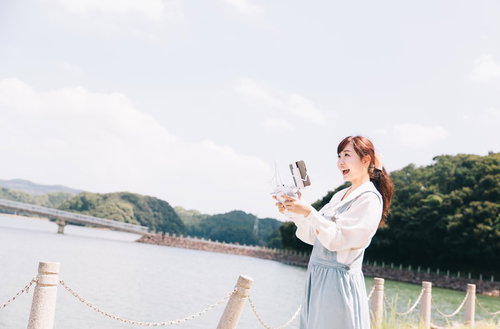 伊万里市の河畔でタブレットを使ってドローンを操縦する女性