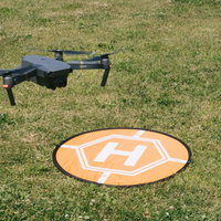芝生に着陸した黒いドローンとオレンジ色のランディングパッドの写真