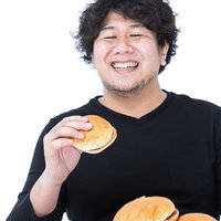 ハンバーガーとフライドポテトの山を前に笑顔で頬張る男性の写真
