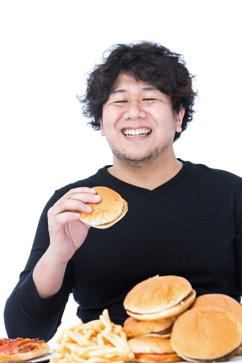 ハンバーガーとフライドポテトの山を前に笑顔で頬張る男性の写真