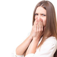 口臭に顔をしかめ手で口を塞ぐ若い女性のリアクションの写真