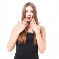 両手を口元に当てて目を大きく開ける驚きの茶髪女性の写真