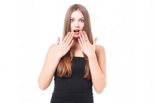 両手を口元に当てて目を大きく開ける驚きの茶髪女性