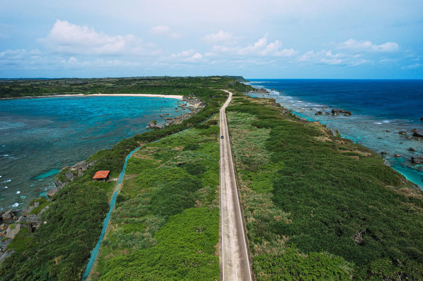 宮古島の平安名埼灯台へ続く一本道をドローンで空撮した写真。左右に海を見ながら走る車