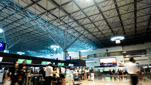 空港ターミナルのチェックインカウンター前で手続きを待つ旅行者たち