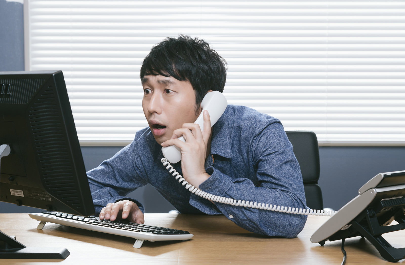 オフィスのデスクで電話をしながらパソコンを操作する男性［モデル：大川竜弥］