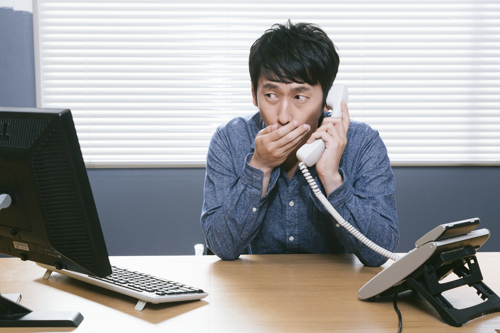 デスクでノートパソコンを見ながら電話をかける男性［モデル：大川竜弥］