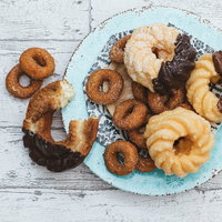 白い皿から溢れ出るカラフルなドーナッツとおやつの写真