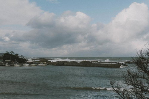 漁船が停泊する静かな漁港と防波堤に打ちつける波