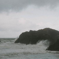 雲間からのぞく青空とは裏腹に横殴りの雨が降る荒れた海の景色の写真