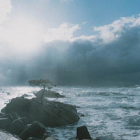 黒雲と青空が対比する荒波の海岸線の写真