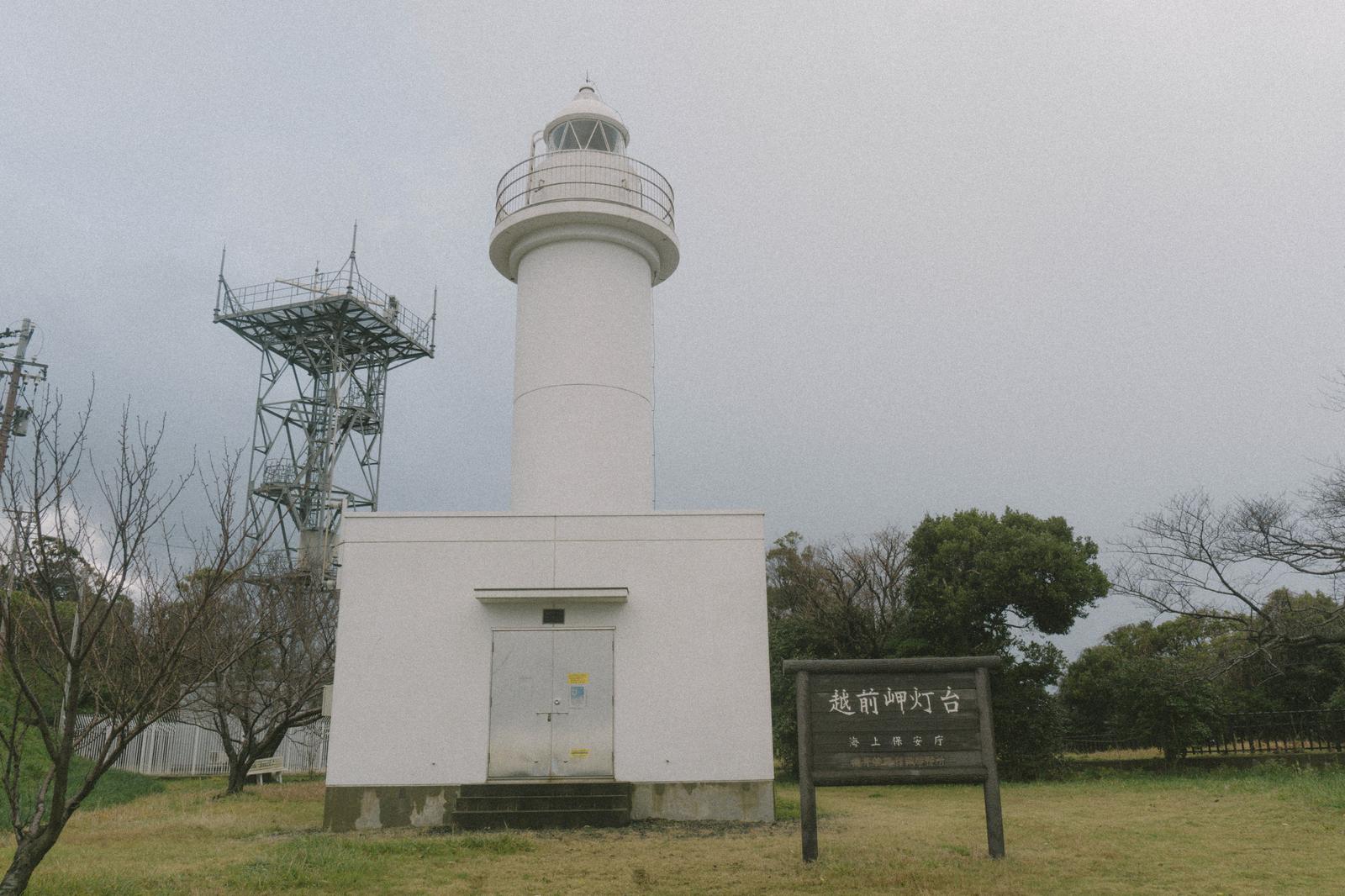 白い灯台と鉄塔が曇り空の下に立つ越前岬灯台の風景
