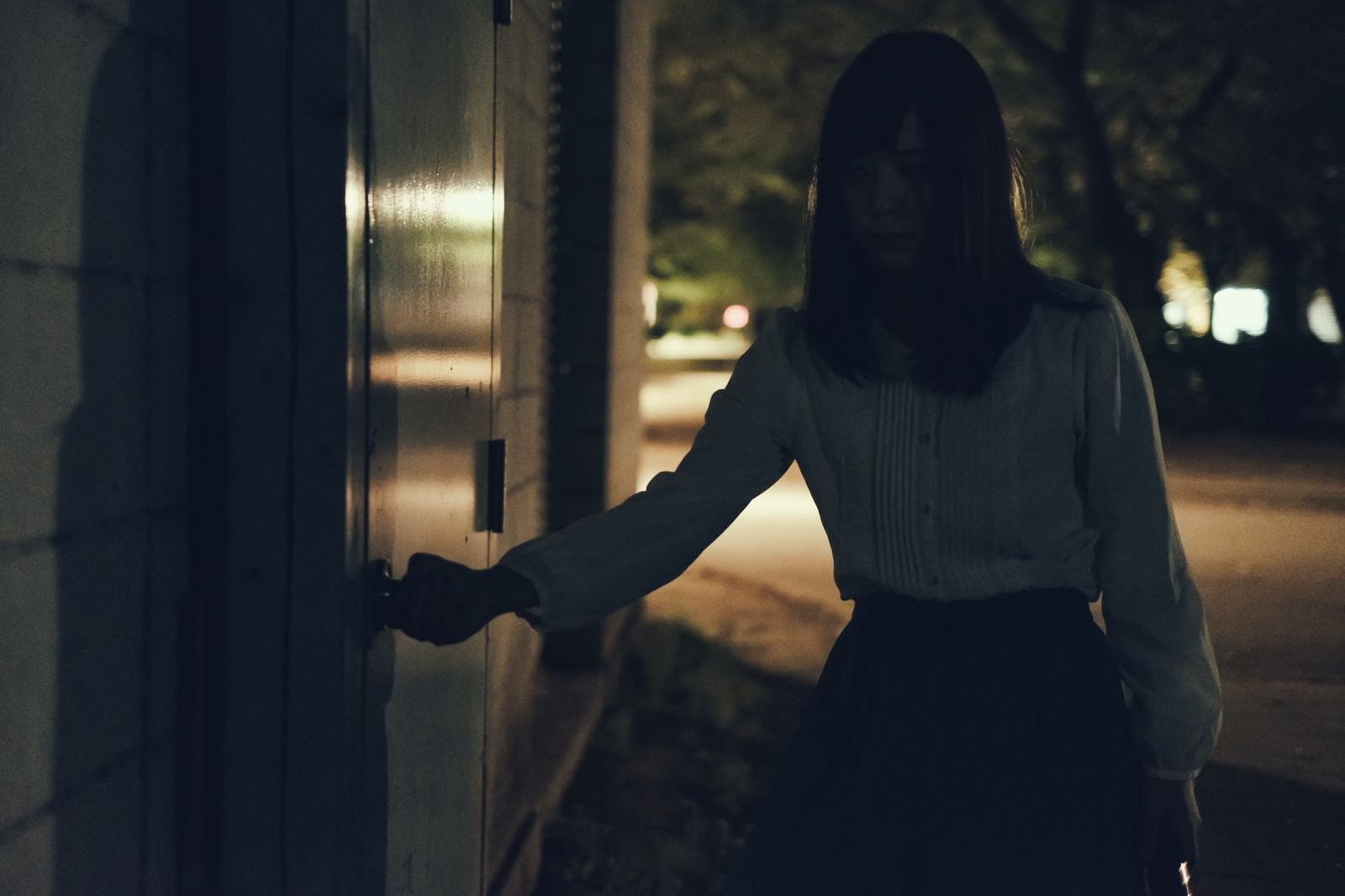 夜の屋外でドアを開ける女性の後ろ姿［モデル：さとうゆい］