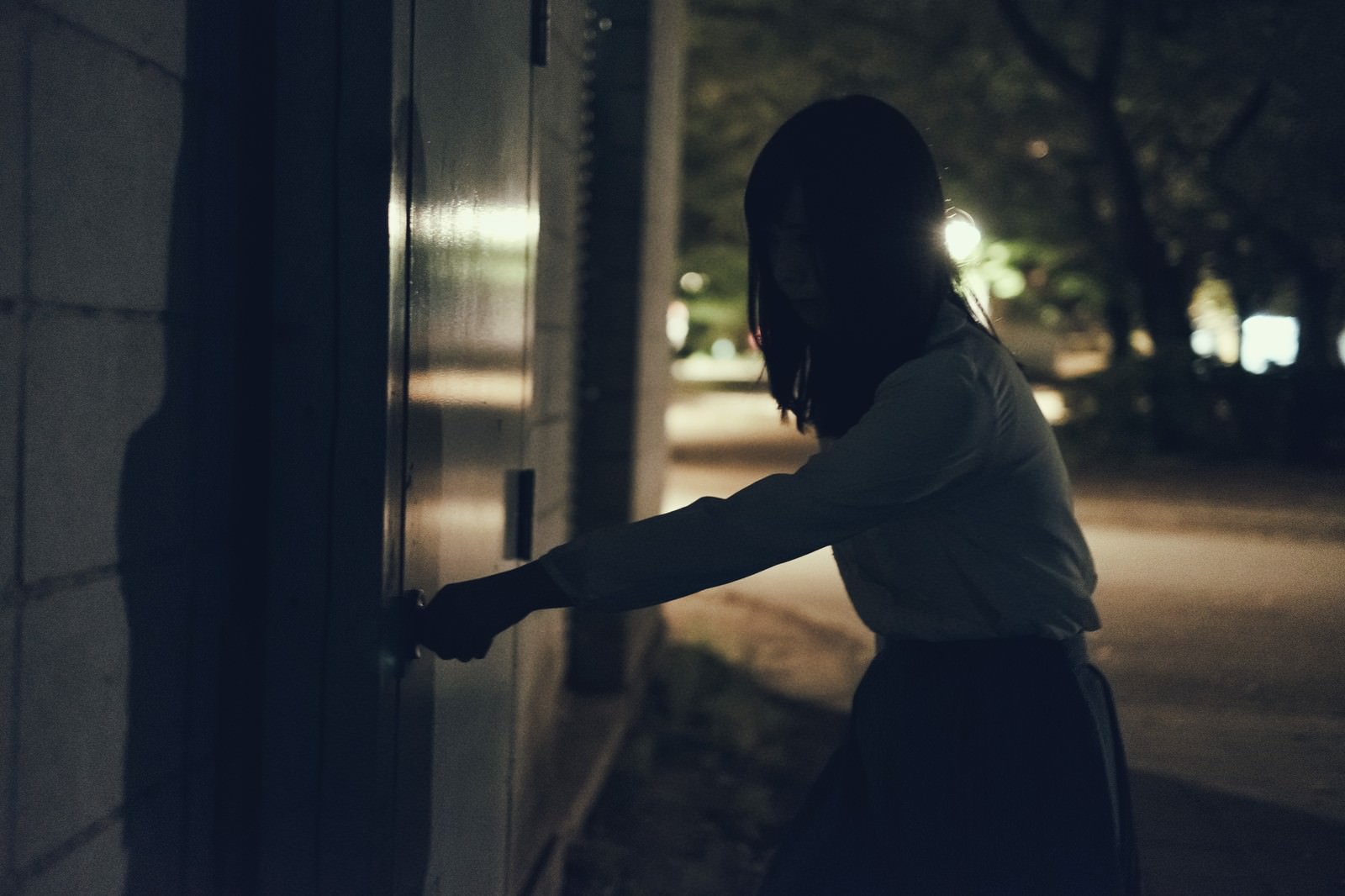 暗い場所で扉のハンドルに手をかける女性のシルエット［モデル：さとうゆい］