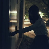 意を決して暗い倉庫の扉に手をかける女性のシルエットの写真