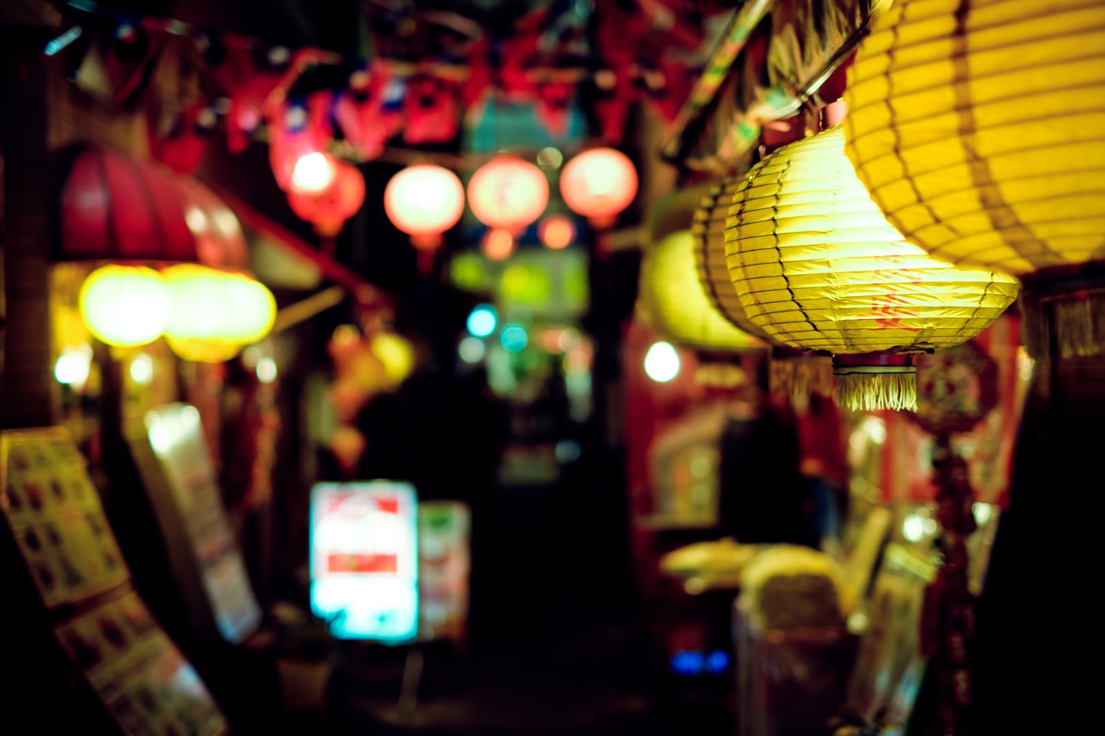 飲み屋街の路地に灯る黄色と赤の提灯が複数下がっている夜間の風景
