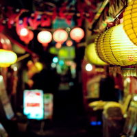 夜の飲み屋街に灯る黄色と赤の提灯と居酒屋の看板の写真