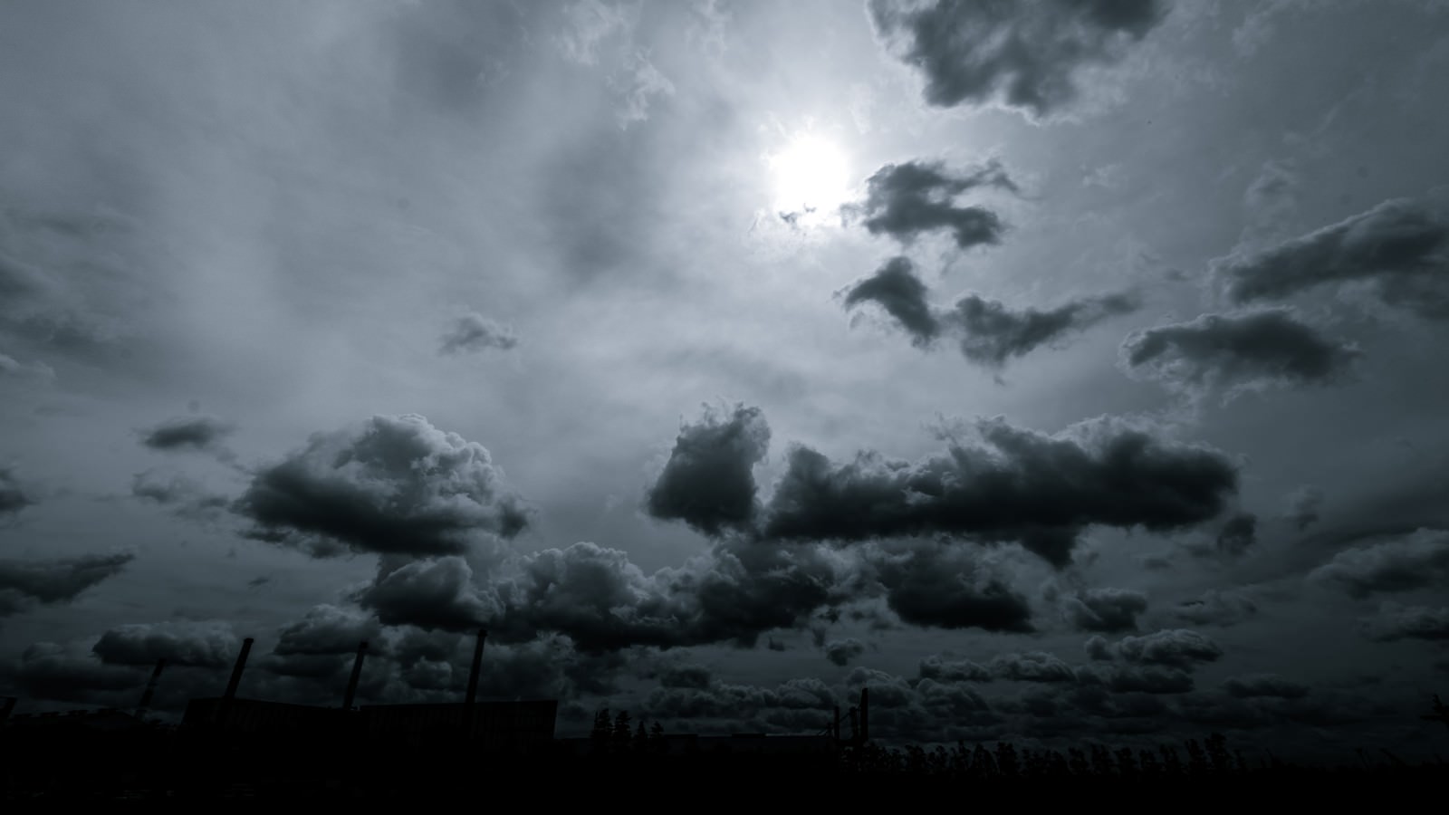 厚い雲の合間から光が漏れるモノクロの空