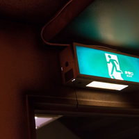 暗い廊下の天井でぼんやりと光る薄暗い非常灯の写真