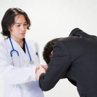 白衣の医師に深く頭を下げて感謝するスーツのサラリーマンの写真