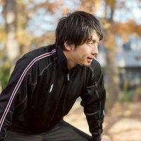 ジャージ姿で足を伸ばしてストレッチの準備運動をする男性の写真