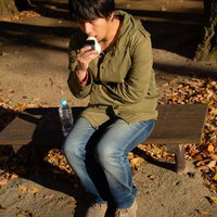 公園のベンチで寂しそうにおにぎりを一人で食べる男性の写真