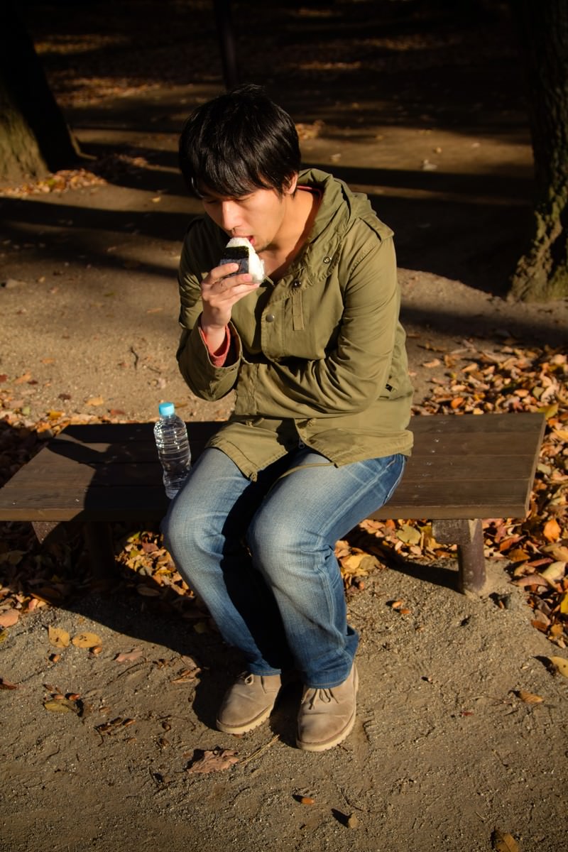 公園で一人おにぎりを食べる男性［モデル：大川竜弥］