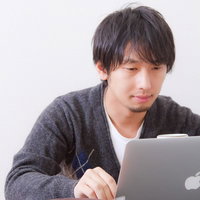 お菓子食べながらパソコンをする男性の写真