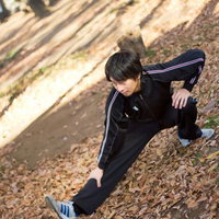 ジャージ姿で片足を伸ばして伸脚のストレッチをする男性の写真