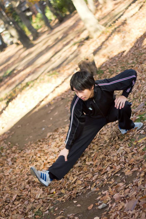 ジャージ姿で片足を伸ばして伸脚のストレッチをする男性