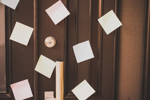 縦溝模様の茶色い木製ドアに複数の白い付箋と金色の鍵穴が写る接写