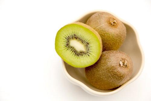 白い皿に載った丸ごとと半分に切ったキウイフルーツ3個