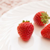 白い皿にイチゴ3つとピンクの花柄の布の写真