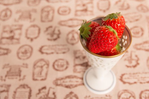 白い脚付きカップに入った赤いイチゴ3個