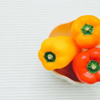白い木目テーブルに置いた黄色とオレンジと赤のパプリカ3個の写真